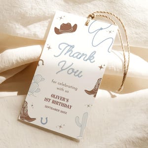 Puede incluir: Una etiqueta rectangular con temática de vaquero. La etiqueta presenta ilustraciones de un sombrero de vaquero marrón, una cuerda, botas, una herradura y un cactus. El texto dice "Thank You" y "for celebrating with us".