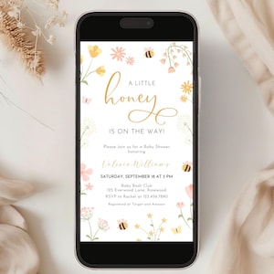 May include: A smartphone displays a baby shower invitation with floral and bee illustrations. The text reads "A Little Honey Is On The Way!" in gold script. Details include the honoree's name, date, time, and location.