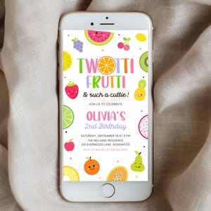 May include: A smartphone displays a colorful birthday invitation. The design features the words "TWOTTI FRUTTI" with fruit illustrations like watermelon, grapes, and kiwi. The invitation is for Olivia's 2nd birthday, with date, time, and location details.