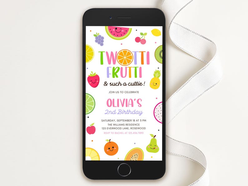 May include: A smartphone displays a colorful birthday invitation with the text "Twotti Frutti & such a cuttie!" and "Olivia's 2nd Birthday." The design features cartoon fruits like watermelon, strawberries, and kiwi. The phone is on a white surface.