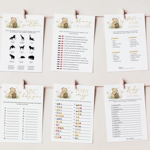 May include: Six baby shower game cards are displayed, each held by a wooden clip on a string. The cards feature a Winnie the Pooh theme with gold text and illustrations. Games include "Animal Gestation," "Mommy or Daddy," and "What's in Your Purse."