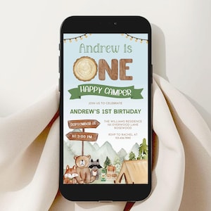 May include: A smartphone displays a digital invitation for Andrew's 1st birthday. The invitation features a camping theme with a bear, fox, and raccoon illustration. Text includes "Andrew is ONE Happy Camper" and event details.