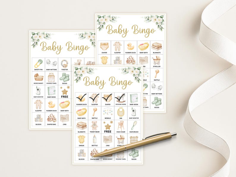 May include: Three Baby Bingo cards with watercolor illustrations of baby items like a rubber duck, crib, and bottle. The cards have a floral design and the words "Baby Bingo" in gold script. A gold pen and white ribbon are also in the image.
