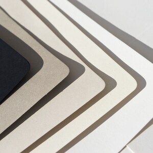 May include: A set of six paper samples in various shades of gray and white, arranged in a fan shape. The darkest shade is black.