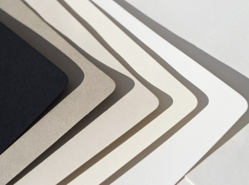 May include: A set of six paper samples in various shades of gray and white, arranged in a fan shape. The darkest shade is black.