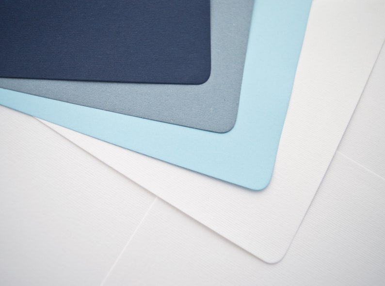 May include: Stack of four paper sheets in shades of blue and white. The top sheet is dark blue, the second is light blue, the third is gray, and the bottom sheet is white.
