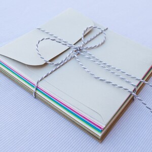 May include: A stack of colorful envelopes tied together with a white twine bow. The envelopes are in various shades of green, blue, pink, and brown.