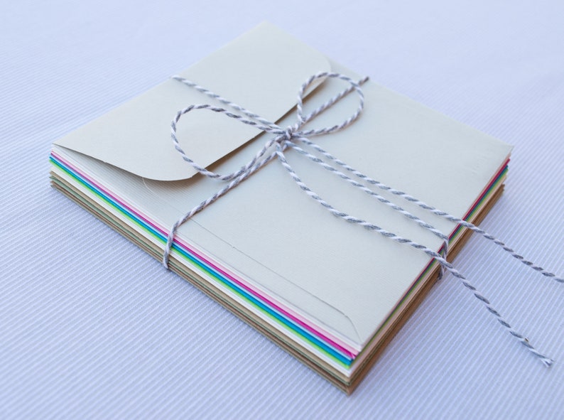 May include: A stack of colorful envelopes tied together with a white twine bow. The envelopes are in various shades of green, blue, pink, and brown.
