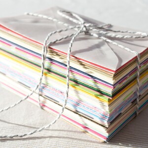 May include: A stack of colorful envelopes tied together with twine. The envelopes are various shades of pink, blue, green, yellow, and white.