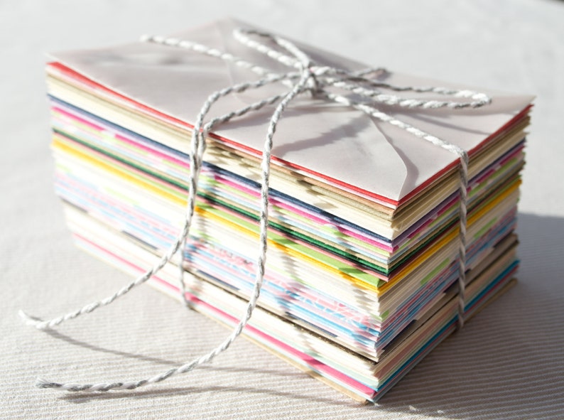 May include: A stack of colorful envelopes tied together with twine. The envelopes are various shades of pink, blue, green, yellow, and white.