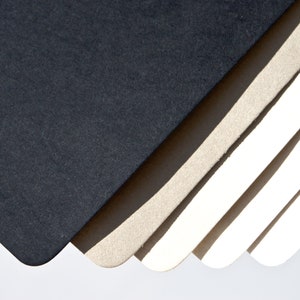May include: A stack of different colored paper sheets, with the top sheet being black, the next sheet being a light brown, and the remaining sheets being white.