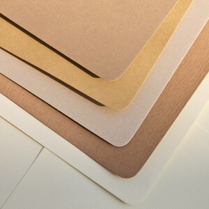 May include: A stack of five different colored paper sheets, with the top sheet being a light brown color, the second sheet being a light gold color, the third sheet being a light gray color, the fourth sheet being a light brown color, and the bottom sheet being a white color.