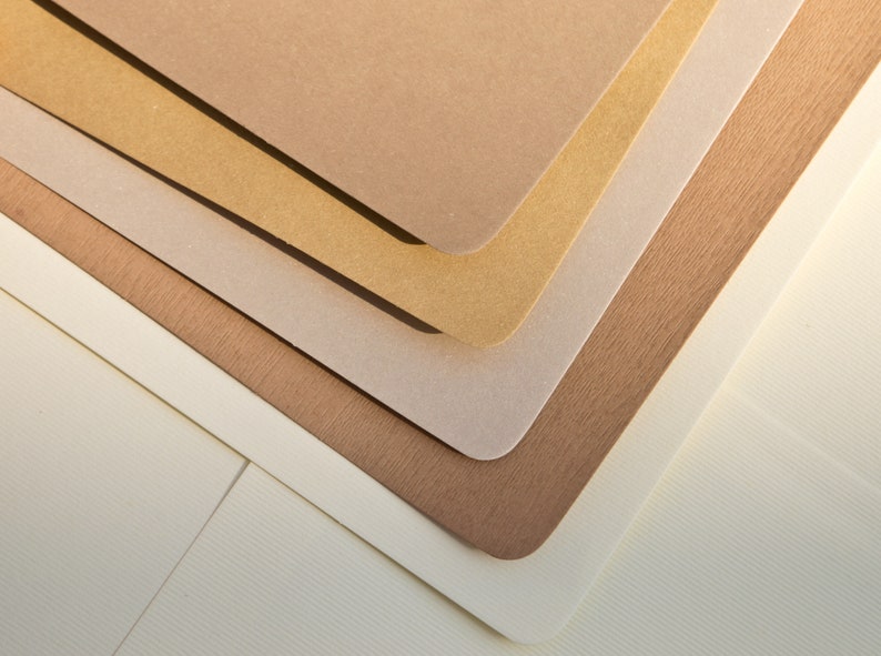 May include: A stack of five different colored paper sheets, with the top sheet being a light brown color, the second sheet being a light gold color, the third sheet being a light gray color, the fourth sheet being a light brown color, and the bottom sheet being a white color.
