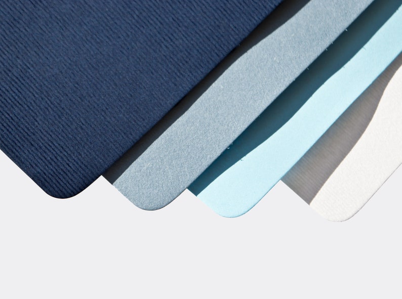 May include: Four pieces of cardstock in shades of blue, gray, and white. The cardstock is arranged in a fan shape, with the darkest blue at the top and the lightest white at the bottom.