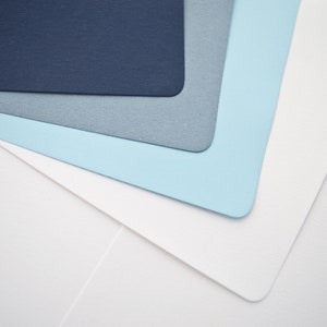 May include: Stack of four paper sheets in shades of blue and white. The top sheet is dark blue, the second is light blue, the third is gray, and the bottom sheet is white.