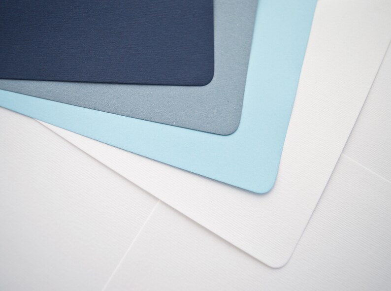 May include: Stack of four paper sheets in shades of blue and white. The top sheet is dark blue, the second is light blue, the third is gray, and the bottom sheet is white.