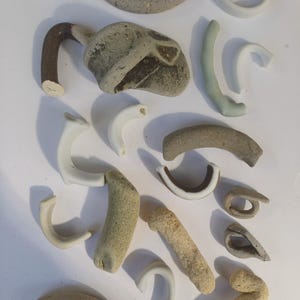 以下が含まれることがあります： 茶色、白、緑など、さまざまな形と色のセラミック陶器の詰め合わせ。陶器は白い表面に並べられています。