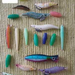 Op de afbeelding: Een verzameling vislokazen in verschillende vormen en kleuren, waaronder groen, blauw, roze en wit. De lokazen zijn gerangschikt op een getextureerd, lichtgroen oppervlak. De tekst "set 1" is linksboven zichtbaar.