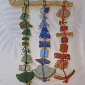 Puede incluir: Un colgante de pared hecho de madera flotante y varias piezas de azulejos de cerámica. Los azulejos están unidos con hilo y son de tonos verdes, azules, rojos y marrones.