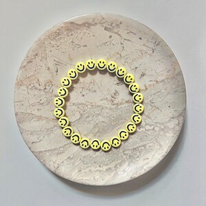 May include: A yellow smiley face necklace on a light beige marble surface.