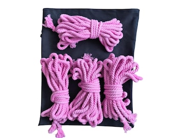 May include: A collection of pink rope bundles and a single bundle on a black fabric. The ropes are tightly wound and tied, with tassels at the ends. The image is set against a white background.