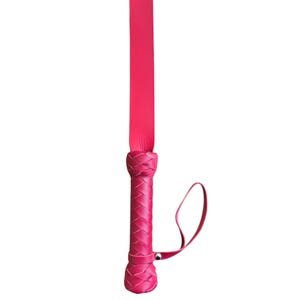 May include: A pink leather whip with a braided handle and a strap.