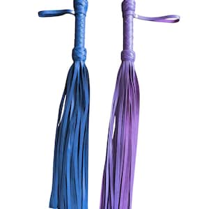 Puede incluir: Dos látigos de cuero con mangos trenzados. Un látigo es azul y el otro es morado.