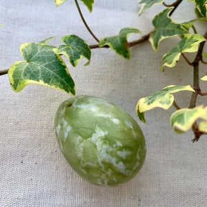 May include: A green and white marbled egg-shaped stone with a small hole in the top.