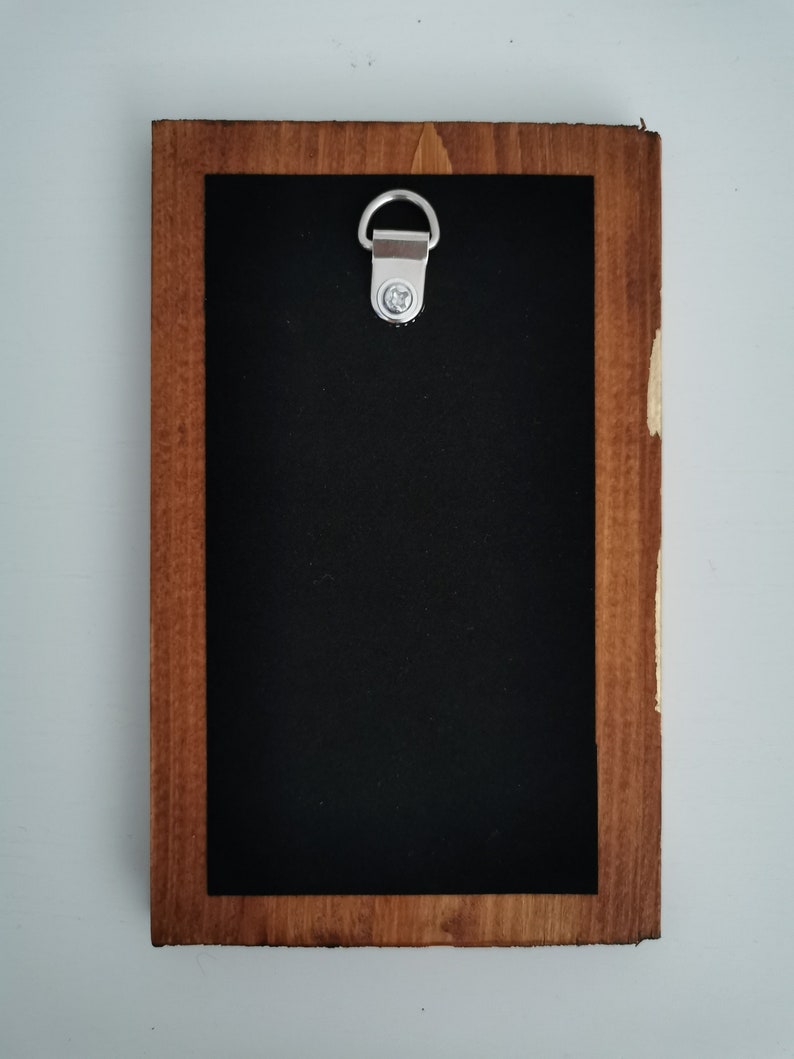 May include: A wooden frame with a black background and a silver hanging hook. The frame is made of dark wood with a light brown stain.