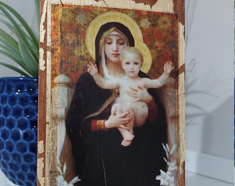 May include: A wooden framed painting of the Virgin Mary holding baby Jesus. The painting is on a gold background with a floral pattern. The frame is distressed and has gold accents.