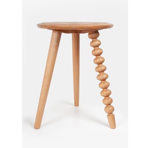 Op de afbeelding: Een houten bijzettafel met drie poten. Eén poot is een reeks verbonden houten kralen.