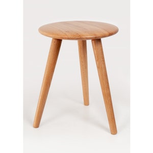 May include: A wooden stool with a round top and three legs. The stool is made of light brown wood and has a natural finish.