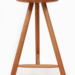 May include: A wooden stool with a round seat and three legs. The legs are connected by a crossbar.