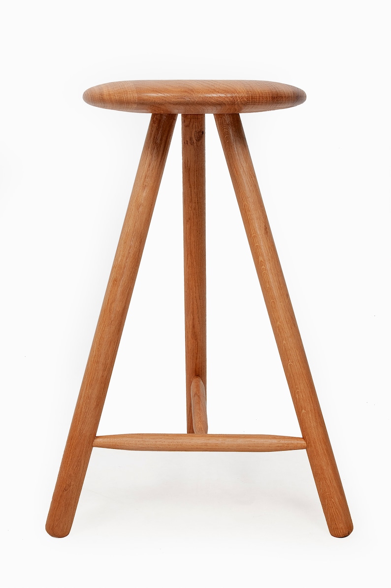 May include: A wooden stool with a round seat and three legs. The legs are connected by a crossbar.