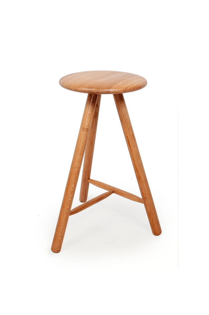 May include: A wooden stool with a round seat and three legs. The stool is made of natural wood and has a simple, rustic design.