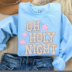 May include: Light blue sweatshirt with a gold glitter design that says "Oh Holy Night" with pink glitter stars.