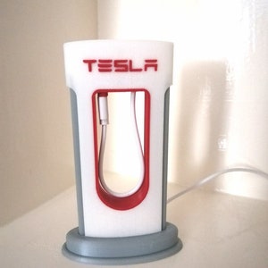 Może przedstawiać: Biało-czerwony model stacji ładowania Tesla wydrukowany w 3D z szarą podstawą. Model ma biały kabel wychodzący z góry.