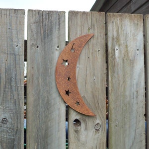 May include: A rusty metal crescent moon with cut-out stars attached to a wooden fence.