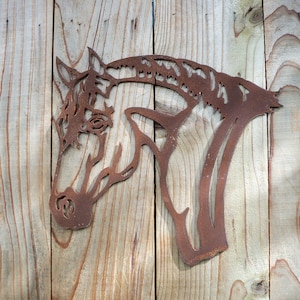 Puede incluir: Una silueta de cabeza de caballo de metal oxidado montada en una superficie de madera. La cabeza de caballo est&aacute; recortada en metal y tiene un dise&ntilde;o detallado.