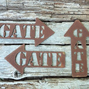 May include: Three rusty metal signs with arrows pointing in different directions. The signs read "GATE" in a rustic font.