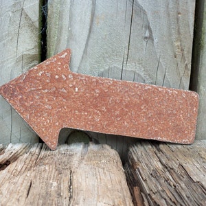 May include: A rusty metal arrow pointing to the left, resting on a weathered wooden surface.