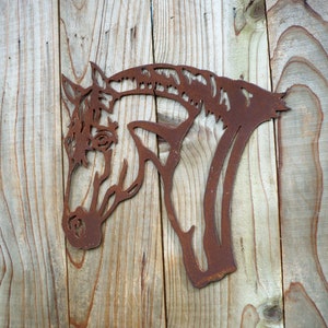 Puede incluir: Una silueta de cabeza de caballo de metal oxidado montada en una superficie de madera. La cabeza del caballo est&aacute; mirando hacia la izquierda y la silueta est&aacute; recortada en un dise&ntilde;o detallado.