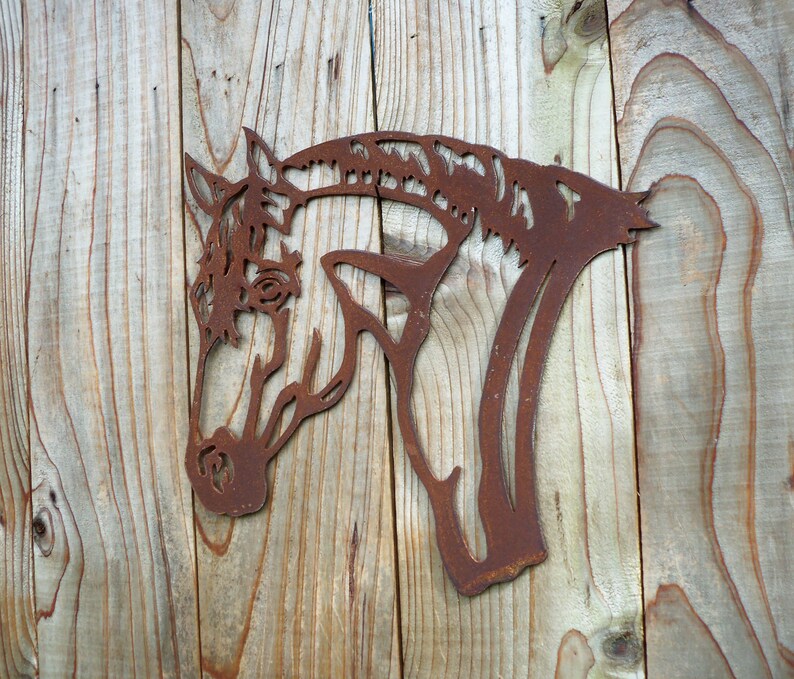 Puede incluir: Una silueta de cabeza de caballo de metal oxidado montada en una superficie de madera. La cabeza del caballo est&aacute; mirando hacia la izquierda y la silueta est&aacute; recortada en un dise&ntilde;o detallado.
