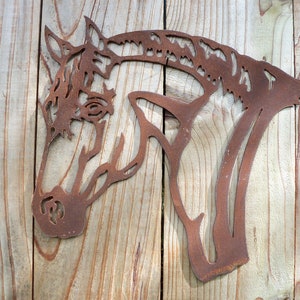 Puede incluir: Una decoraci&oacute;n de pared de metal oxidado en forma de cabeza de caballo. La cabeza de caballo est&aacute; mirando hacia el lado derecho de la imagen. La cabeza de caballo est&aacute; montada en una superficie de madera.