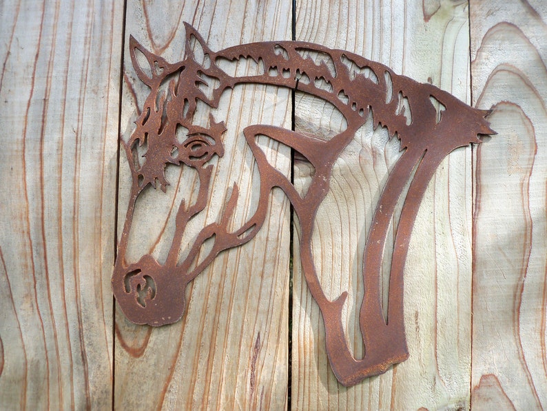 Puede incluir: Una decoraci&oacute;n de pared de metal oxidado en forma de cabeza de caballo. La cabeza de caballo est&aacute; mirando hacia el lado derecho de la imagen. La cabeza de caballo est&aacute; montada en una superficie de madera.