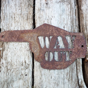 May include: A rusty metal sign shaped like a pointing hand with the words "WAY OUT" cut out. The sign is attached to a weathered wooden surface.