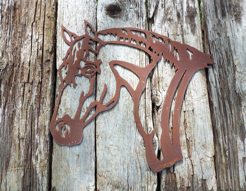 Puede incluir: Una silueta de cabeza de caballo de metal oxidado, montada sobre una superficie de madera desgastada. La cabeza del caballo est&aacute; mirando hacia el lado izquierdo de la imagen.