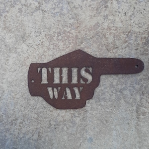 May include: A rusty metal sign shaped like a hand pointing right with the words "THIS WAY" cut out.