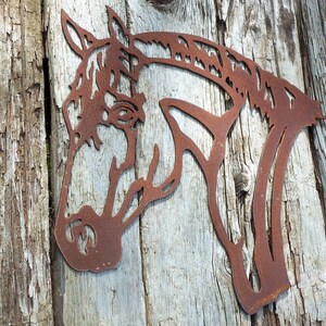 Puede incluir: Una silueta de cabeza de caballo de metal oxidado montada sobre una superficie de madera desgastada.