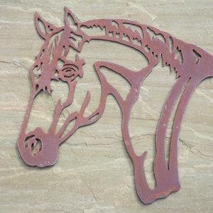 Puede incluir: Una decoraci&oacute;n de pared de metal oxidado en forma de silueta de cabeza de caballo. La cabeza del caballo est&aacute; mirando hacia el lado derecho de la imagen. El metal es de color marr&oacute;n oscuro con una textura rugosa.